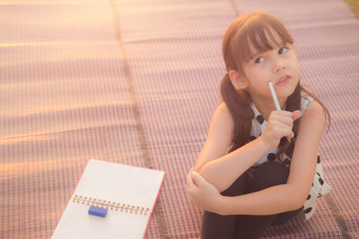 Thoughtful girl sitting by book on mat