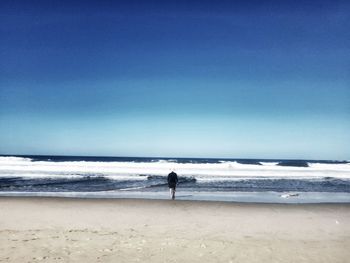 Rear view of man walking at sandy beach against blue sky