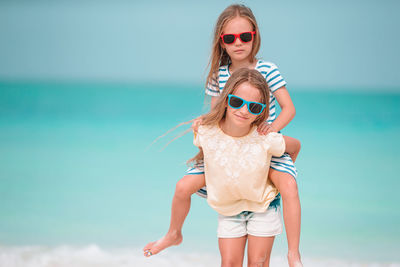 Portrait of girl carrying sister on back against sea
