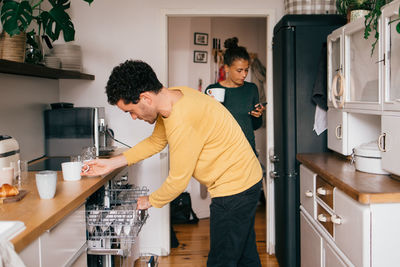 Mid adult man removing cup from drawer below kitchen counter at home