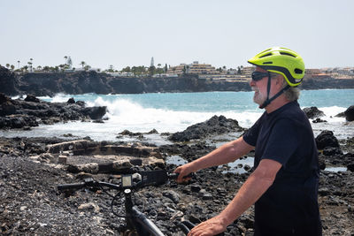 Man standing on bicycle by sea against clear sky