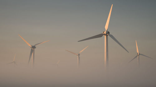Giant windmills rising out of the mist. theme of green energy. suitable for wallpaper or screensaver