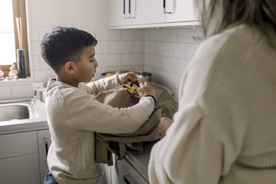 Autistic boy putting banana in bag standing by mother at home