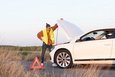 Angry man checking his broken car engine to fix it for going back home after a long trip day