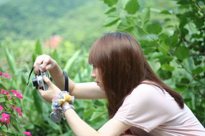 Side view of young woman photographing flowers