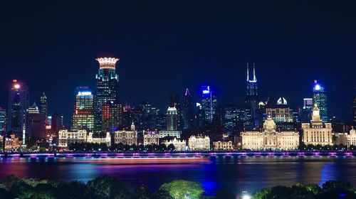 Illuminated buildings by river against sky in city at night