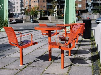 Empty chairs and tables on sidewalk by buildings in city