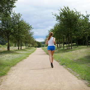 Rear view of woman jogging on footpath amidst field