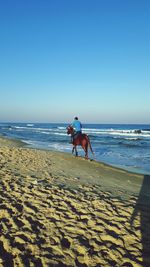 Man riding horse on beach against clear sky