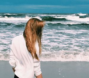 Rear view of woman standing at beach against sky