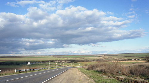 Road passing through landscape against cloudy sky