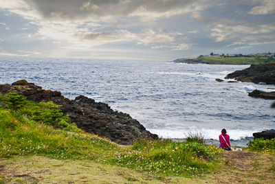 Woman sitting at beach against sky