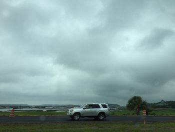 Road passing through field against cloudy sky