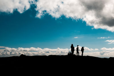 Silhouette people standing on land against cloudy sky