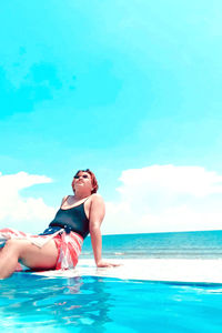 Full length of young woman in swimming pool against sea