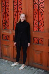 Portrait of young woman standing against door