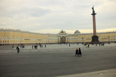 People in front of historical building against cloudy sky
