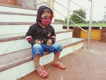 Full length of cute boy wearing flu mask sitting on staircase