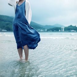 Low section of woman standing in water by shore