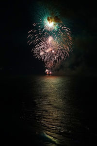 Low angle view of firework display over sea against sky at night