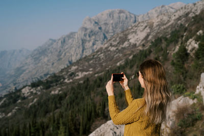 Side view of woman photographing against mountain
