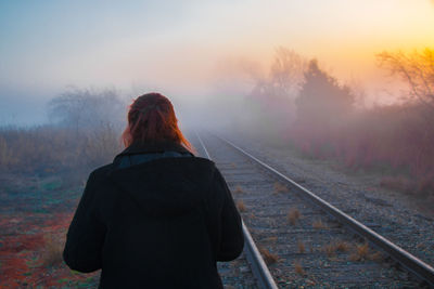 Rear view of person standing by railroad track during sunset