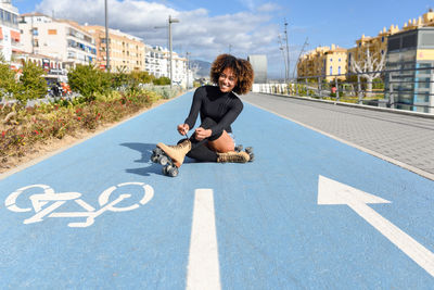 Portrait of smiling woman wearing roller skates while sitting on bicycle lane in city