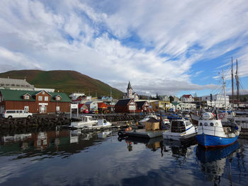 Sailboats moored in harbor by buildings against sky in city