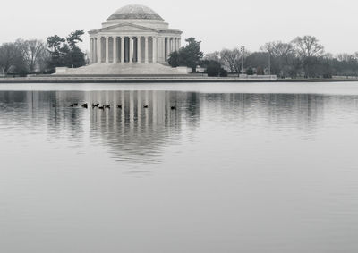 Birds swimming in tidal basin by thomas jefferson memorial against sky