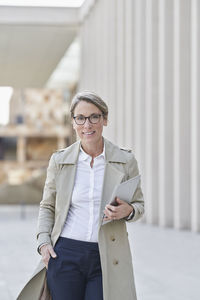 Confident businesswoman holding tablet pc standing with hand in pockets