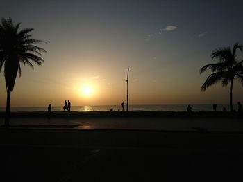 Silhouette palm trees on beach against sky during sunset