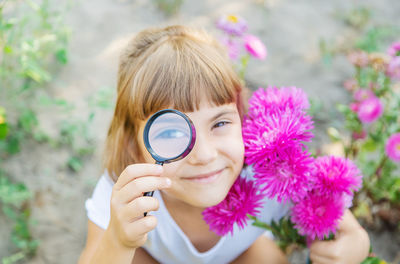 Portrait of smiling girl holding flowers looking through magnifying glass