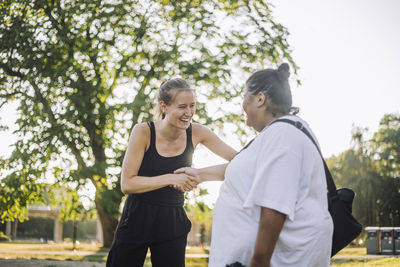 Happy young woman doing handshake with oversize woman at park