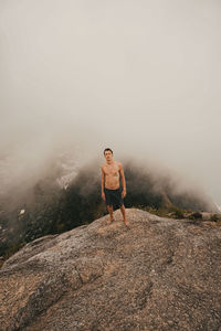 Young man standing on rock against sky