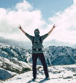 Man with arms outstretched standing on snow covered mountains against sky