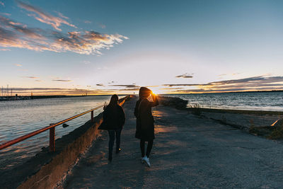 Rear view of women on beach against sky during sunset