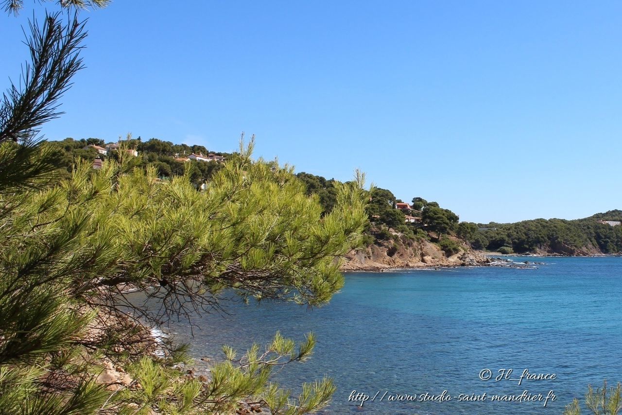 water, clear sky, tranquil scene, tranquility, scenics, blue, beauty in nature, mountain, nature, sea, copy space, tree, idyllic, cliff, non-urban scene, plant, day, landscape, rock formation, lake