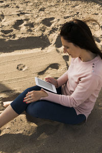 High angle view of woman using digital tablet while sitting at beach