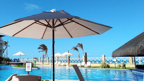 Deck chairs by swimming pool against clear blue sky