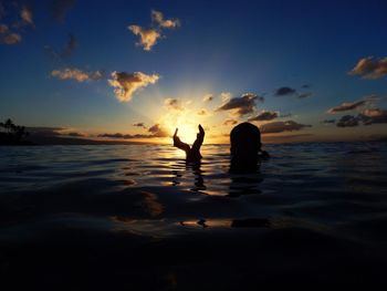 Silhouette people sitting by sea against sky during sunset