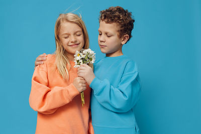 Smiling girl with boy holding flowers against blue background