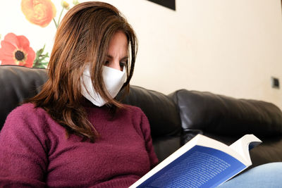 Portrait of teenage girl sitting on sofa at home trading book during coronavirus quarantine