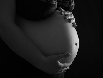 Midsection of pregnant woman standing against black background