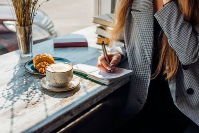 A young woman is sitting at a table by the window and writing in a notebook. 