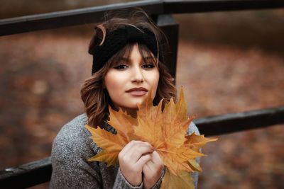 Close-up portrait of a young woman holding autumn leaf
