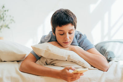 Attractive young woman lying in bed uses mobile phone for social media.