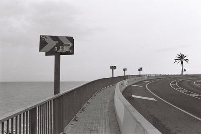 Road sign by sea against sky