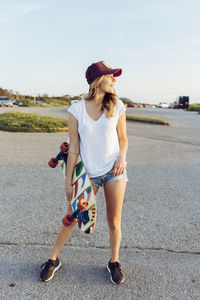 Cheerful woman looking away outdoors while holding skateboard