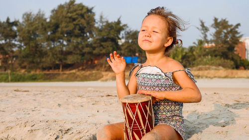 Cute girl playing drum while sitting at beach