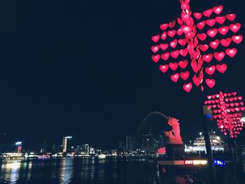 Illuminated ferris wheel by buildings against sky at night